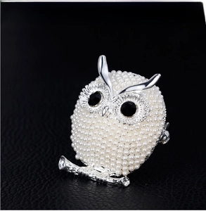 Close-up of owl brooch with white pearls and black gemstone eyes on silver base