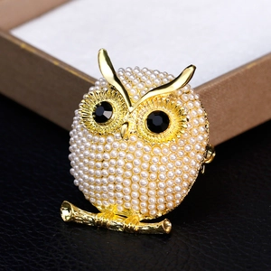 Elegant gold owl brooch with white pearls and black gemstones on black leather background