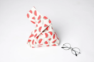 Detail of canvas wrist bag with watermelon print and knots, shown with round glasses