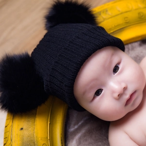 Gros plan sur un bonnet en tricot noir pour bébé avec deux grands pompons en fourrure