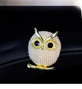 Detailed view of owl brooch with white pearls and gold base on dark background
