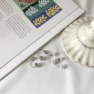 Detail of minimalist C-shape earrings with white pearls and silver beads on a magazine