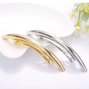 Minimalist curved metal spring hair clips in gold and silver finish on a ceramic plate