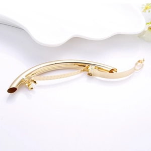 Close-up of a polished gold curved metal hair clip on an elegant white ceramic plate