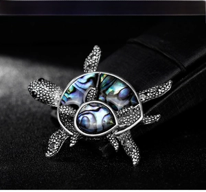 Macro shot of silver turtle brooch featuring natural abalone shell inlay and black stones