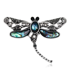 Silver dragonfly brooch with dark crystals and abalone shell inlays on white background