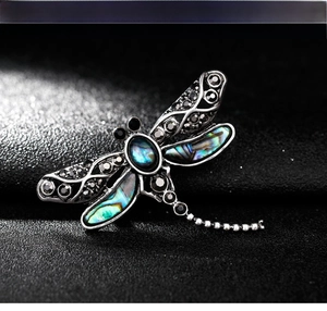 Macro detail of retro dragonfly brooch featuring natural abalone shell and black rhinestones
