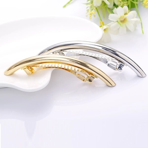 Close-up of polished gold and silver curved metal spring hair clips on a white plate
