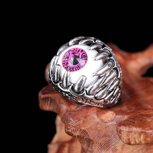 Detailed view of gothic evil eye ring with pink iris set on rustic wooden base