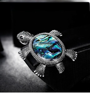 Detailed close-up of a silver turtle brooch with vibrant abalone shell inlay on the back