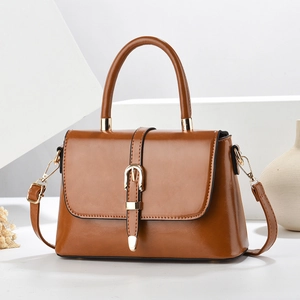 Elegant caramel leather crossbody bag with top handle and gold clasp on a minimalist display