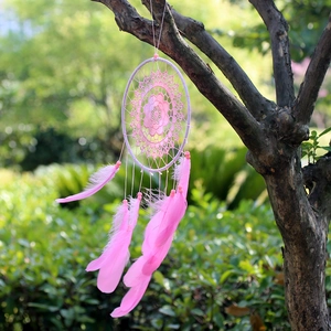 Handmade pink dream catcher with goose feathers and floral net hanging on a tree branch