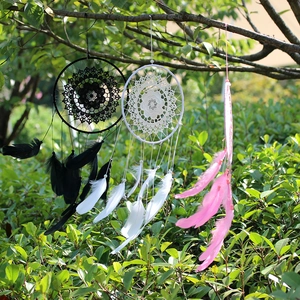 Three handmade goose feather dreamcatchers in black, white, and pink hanging on tree branches