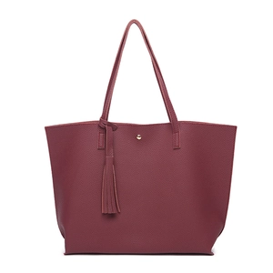 Close-up of burgundy lychee grain leather tote bag featuring a gold metal buckle and tassel