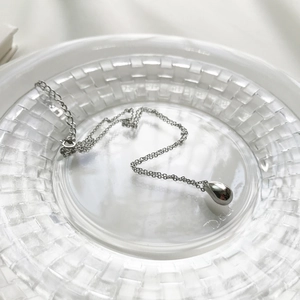 Polished silver teardrop pendant on a fine chain displayed on a textured glass tray