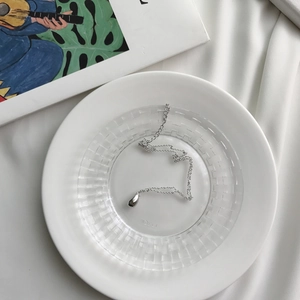 Detail of a polished silver teardrop pendant necklace on a glass dish for jewelry