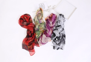 Flat lay of four lightweight leaf-patterned scarves in red, green, purple, and black
