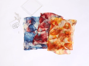 Detailed view of lightweight chiffon scarves with leaf prints in blue, red, and orange