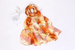 Detail of thin orange chiffon silk scarf with leaf patterns on minimalist white background