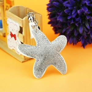 Starfish bag charm with sparkling rhinestones and white tassels on a yellow background