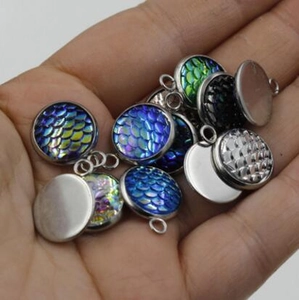 Polished stainless steel round pendant bases with mermaid scale patterns held in palm