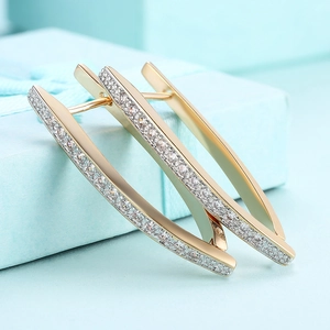 Macro detail of gold-tone earrings with micro-paved white zircons on a blue gift box