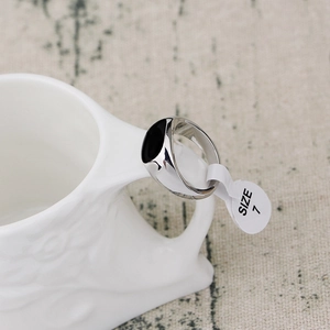 Macro shot of silver ring with black oval inlay hanging on ceramic cup with size 7 tag