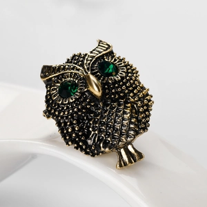 Vintage owl brooch in antique gold finish with green crystal eyes on a white ceramic stand