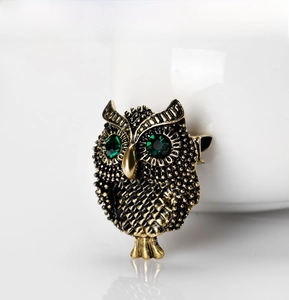 Close-up of vintage alloy owl brooch with green rhinestone eyes and feather textures
