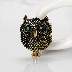 Vintage gold owl brooch with sparkling green gemstone eyes on white ceramic surface