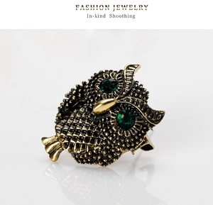 Macro view of vintage owl brooch featuring green gemstone eyes and textured gold finish