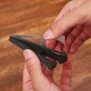 Detail of self-adhesive black foam letter E with backing paper being removed by hand