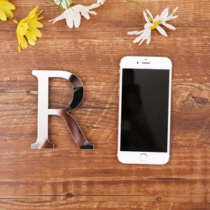 Silver mirror acrylic letter R on wood background with a smartphone for scale