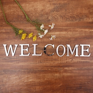 Close-up of mirror silver acrylic WELCOME letters on dark wood with white daisies