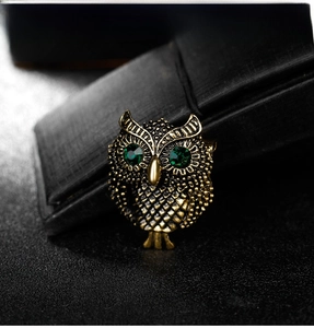 Detailed close-up of owl brooch in vintage gold finish with green gemstone eyes