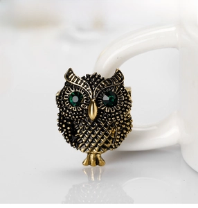 Macro detail of retro owl brooch in antique gold finish with green crystal eyes