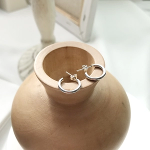 Detail of S925 sterling silver geometric C-shape stud earrings on a wooden bowl edge