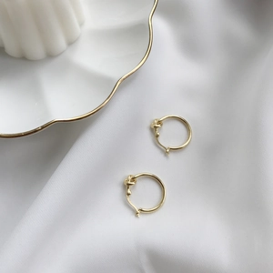 Detailed close-up of gold knotted hoop earrings on white silk and porcelain plate