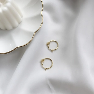Detail of gold-plated S925 silver knotted hoop earrings on elegant white silk fabric