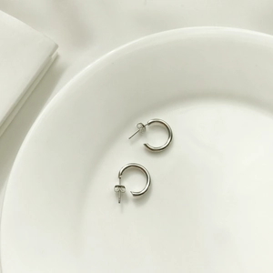 Close-up of minimalist S925 sterling silver C-shaped hoop earrings on white ceramic tray