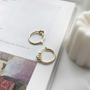 Close-up of golden knotted hoop earrings placed on an art book for a French chic style