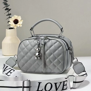 Close-up of gray quilted crossbody bag with triple zippers and LOVE woven strap