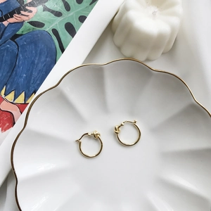 Detail of gold-colored knotted hoop earrings displayed on a refined ceramic plate