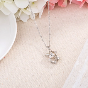 Close-up of silver hollow bow and arrow pendant with a pearl accent on beige fabric