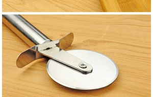 Macro detail of stainless steel pizza cutter wheel with finger guard on wooden surface