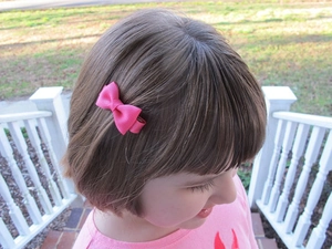 Pink ribbon bow hair clip worn by a child in an outdoor setting with a natural grass background