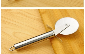 Macro shot of stainless steel pizza cutter wheel on a wooden cutting board