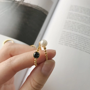 Detail of gold bead rings featuring a black zircon stone and a white pearl on a hand