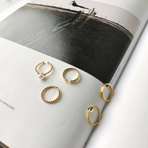 Artistic lifestyle view of 5-piece gold rings set with pearl and black stone on a magazine