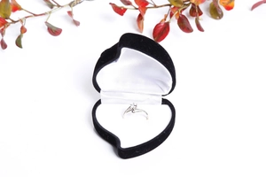 Close-up of a silver twist-band diamond ring inside a black heart-shaped velvet box
